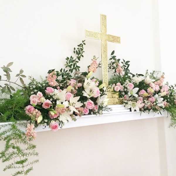Pink and white floral arrangement with lilies and roses around a gold cross