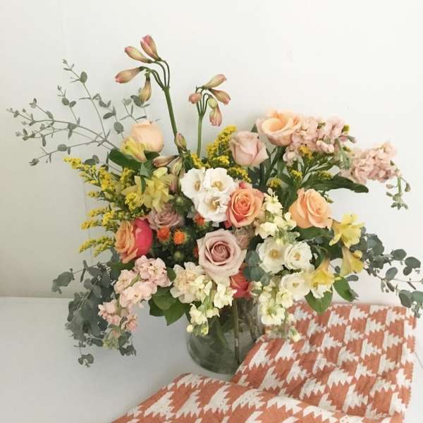 Mixed bouquet of pastel roses, orchids, and yellow filler flowers in a glass vase