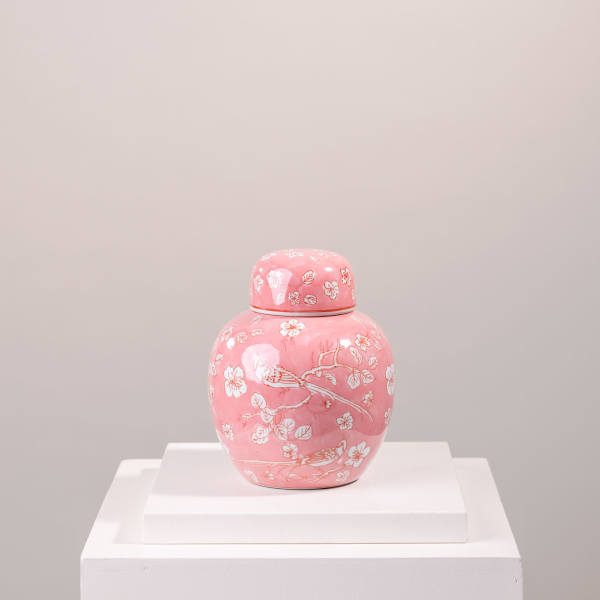 Pink ceramic jar with floral and bird pattern on a white pedestal