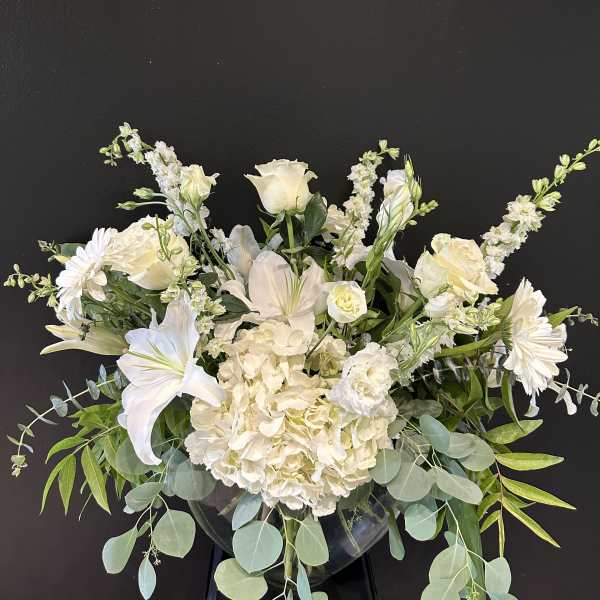 White floral arrangement in a clear vase with lilies, roses, and daisies