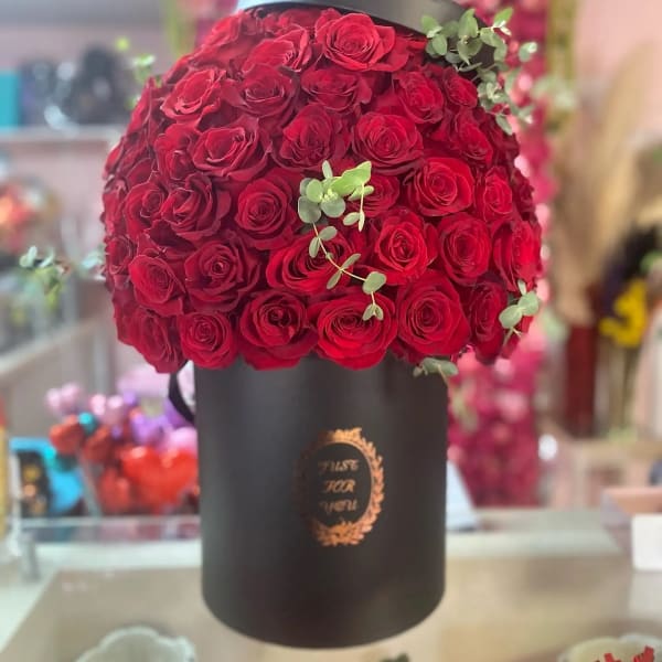 Red roses arranged in a black hatbox with small eucalyptus sprigs