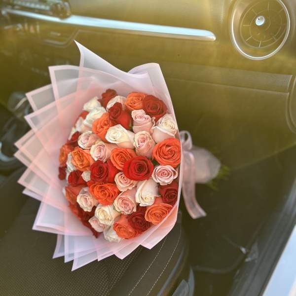 Bouquet of pink, red, and orange roses wrapped in pale pink paper