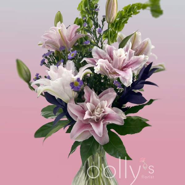 Pink and white lilies in a clear glass vase with purple accents