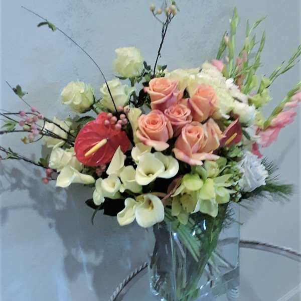 Mixed bouquet of peach roses, white calla lilies, and pink anthurium in a glass vase