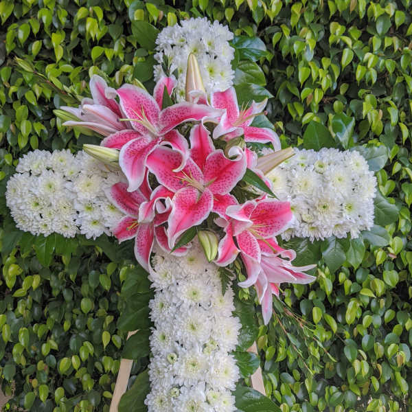 Pink lilies and white chrysanthemums arranged in a cross on a stand