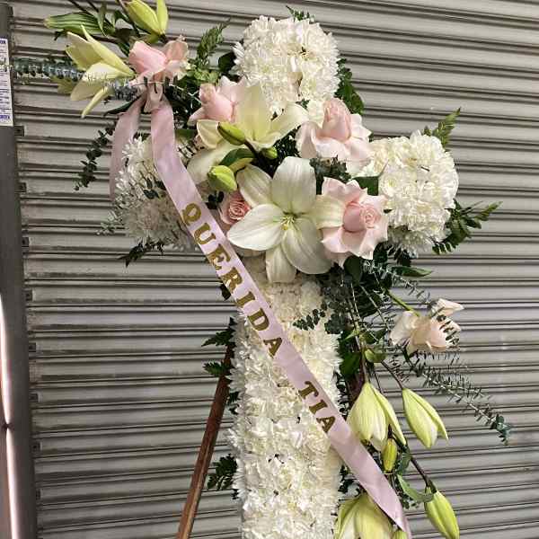 Standing floral cross with white flowers, lilies, and pink ribbon on an easel