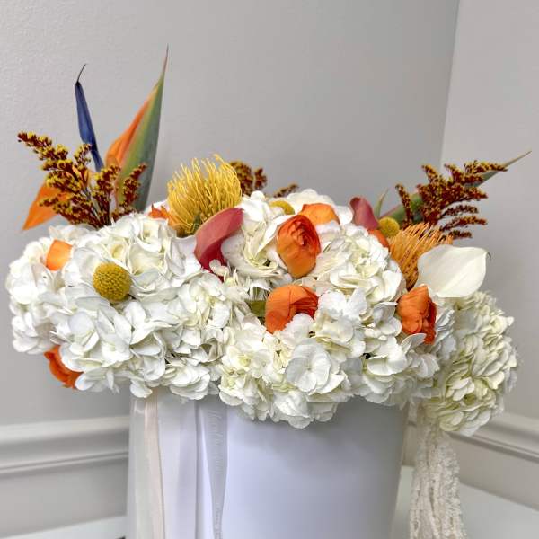 White floral arrangement with orange accents in a round white box