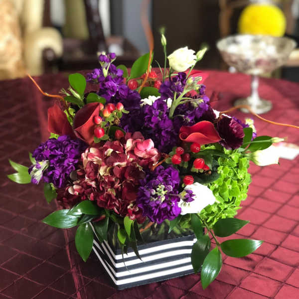 Mixed purple and red floral arrangement in a striped square box