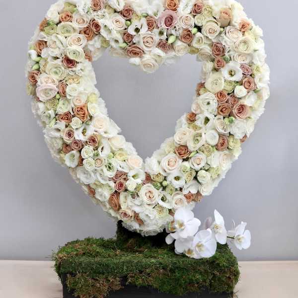 Heart-shaped standing wreath of ivory and blush roses on a moss-covered base with white orchids at the bottom