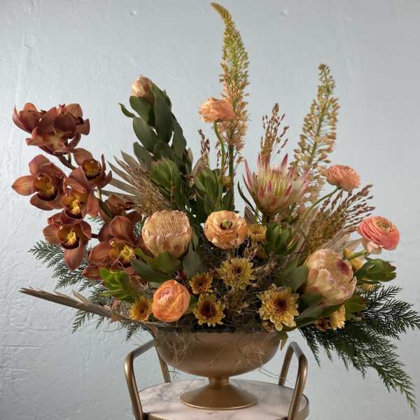 Rust-toned floral arrangement in a gold pedestal bowl