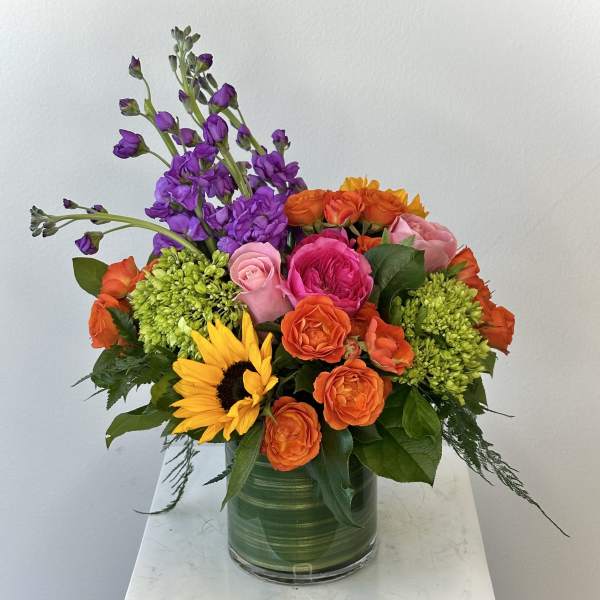 Colorful bouquet with sunflowers, roses, and purple blooms in a glass vase