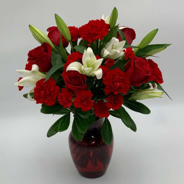 Red roses, white lilies, and carnations in a red glass vase