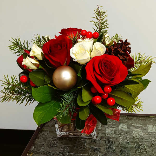Red and white roses in a glass vase with pine sprigs and berries