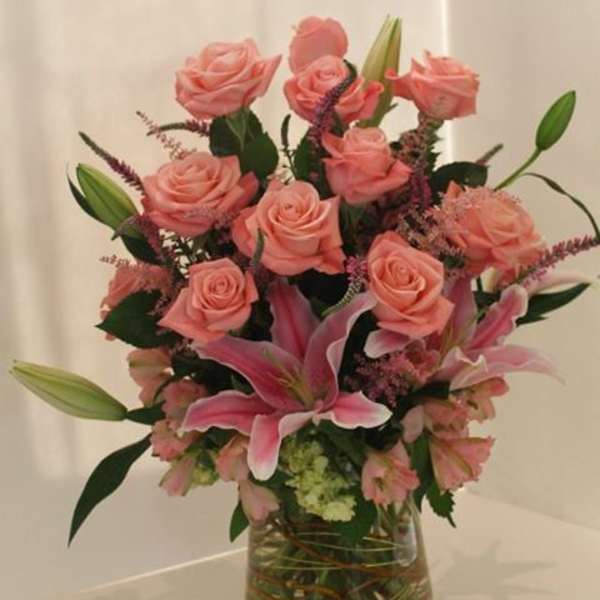 Arrangement of pink roses and lilies in a clear glass vase with a soft, romantic look