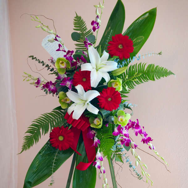 Standing floral spray with red gerberas, white lilies, and purple orchids