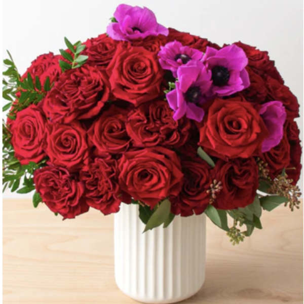 Red roses and purple flowers arranged in a white vase