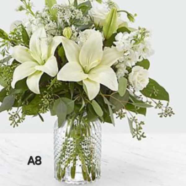 White lilies and mixed white flowers in a clear glass vase