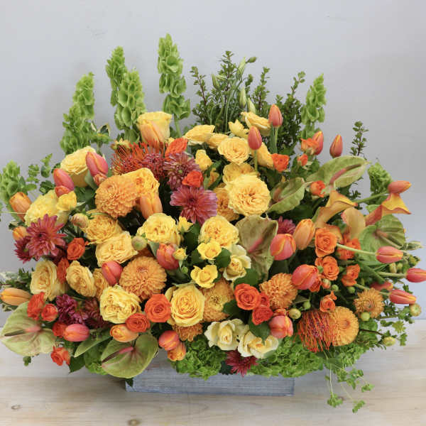 Tall yellow and orange floral arrangement with roses, tulips, and mums in a rectangular container