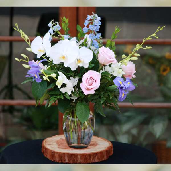 Mixed bouquet of orchids, roses, and blue flowers in a glass vase