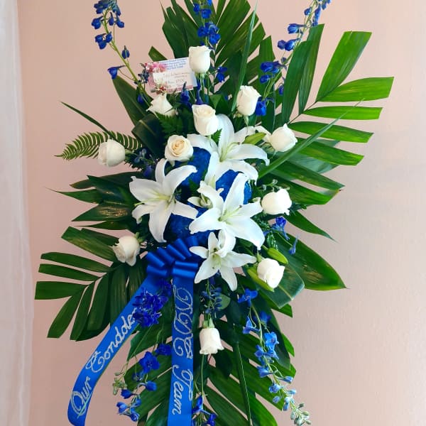 Tall standing floral spray with white lilies, white roses, and blue flowers on an easel.