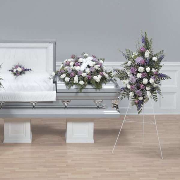 Funeral casket surrounded by white and purple floral sprays