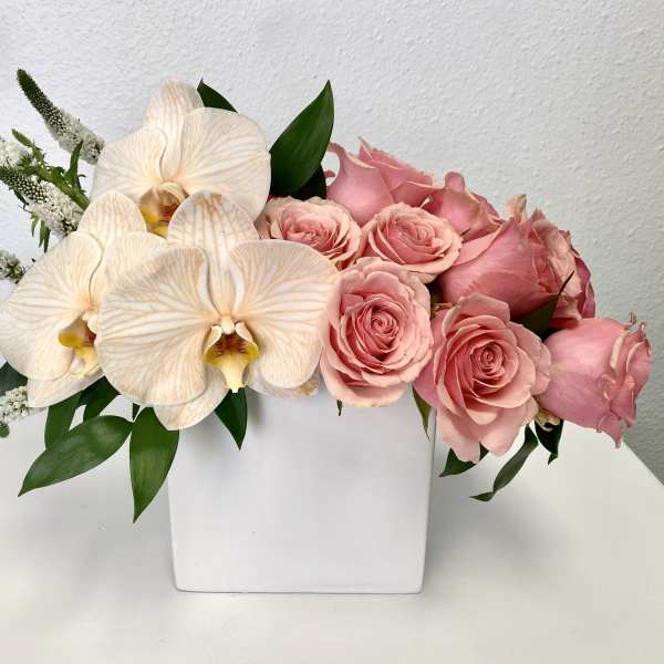 Pink roses and white orchids arranged in a white square vase