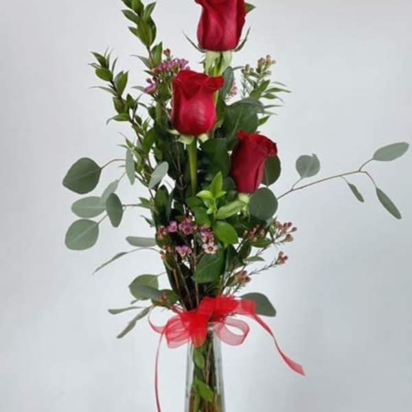 Tall vase arrangement of red roses with greenery and a red ribbon