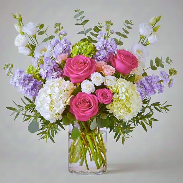 Bouquet of pink roses, white blooms, and lavender flowers in a clear glass vase