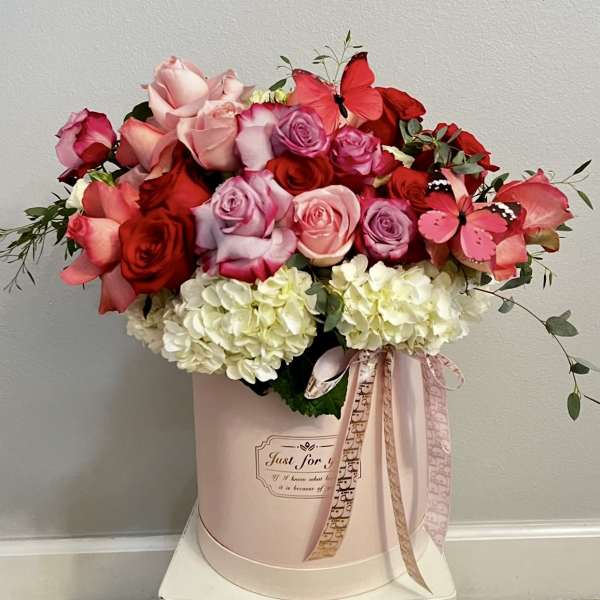Pink and red roses arranged in a pale pink hat box with ribbon.