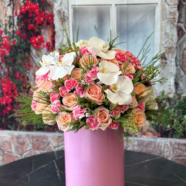 Pink and peach bouquet with white orchids in a tall pink vase