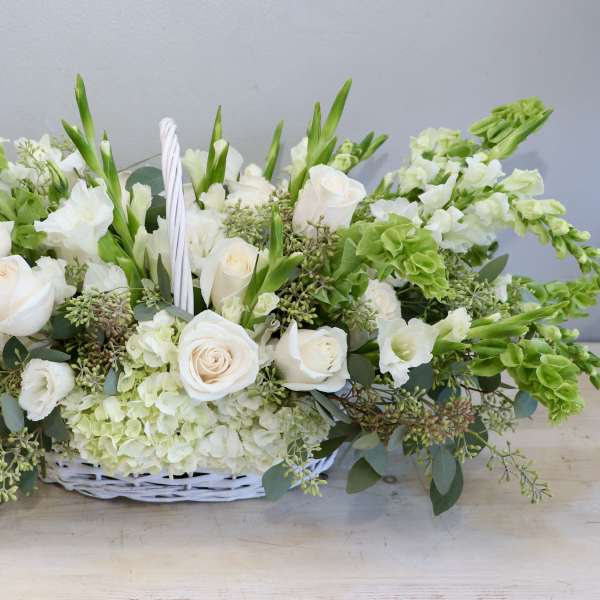 Low white and green floral basket with white roses, hydrangeas, and bells of Ireland