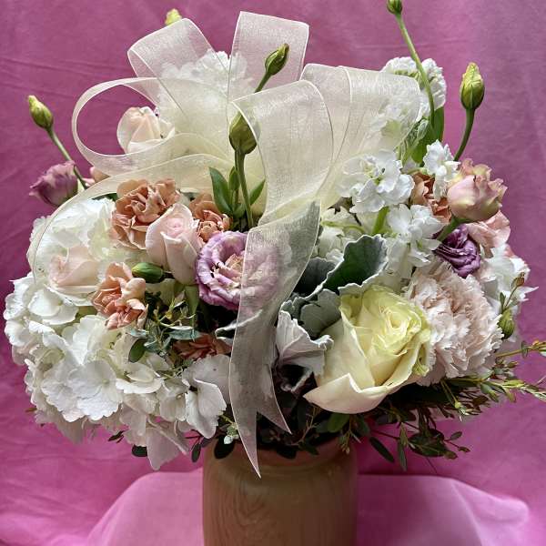 Pastel bouquet of roses, carnations, and white blooms in a wooden vase with ribbon