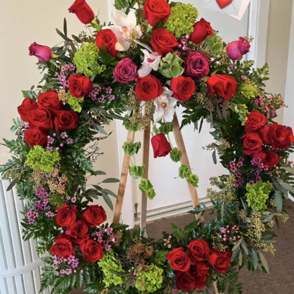 Large floral wreath on an easel with red roses and green accents
