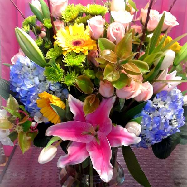 Mixed bouquet in a glass vase with pink lilies, roses, hydrangeas, and yellow daisies
