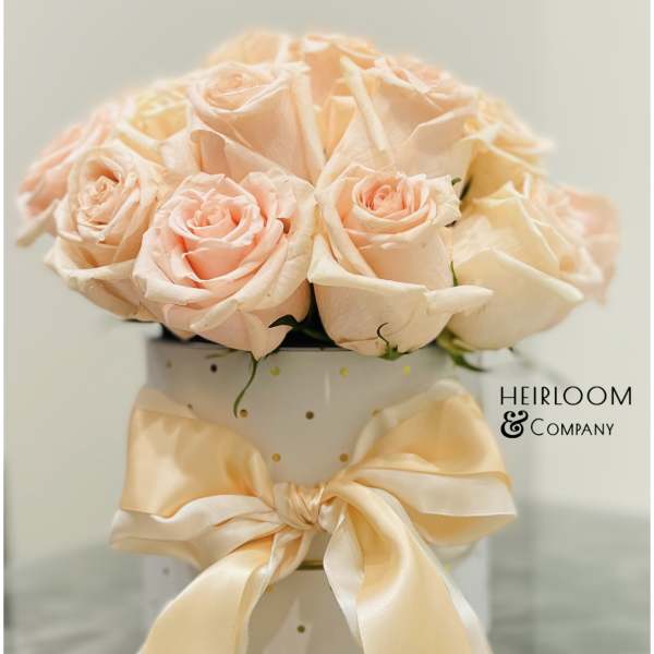 Peach roses arranged in a white polka-dot hatbox with a satin bow