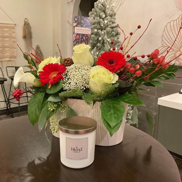 Holiday floral arrangement with red gerbera daisies, cream roses, and a candle in front