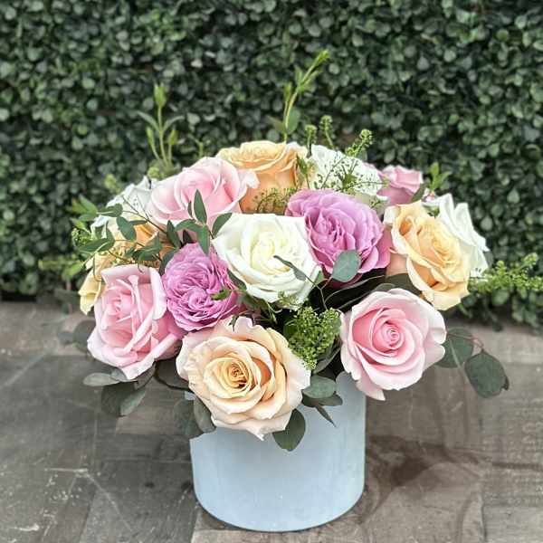 Pastel roses arranged in a light blue box with greenery