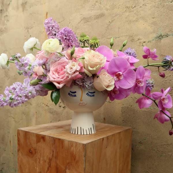 Pink and lavender flowers arranged in a face-shaped vase