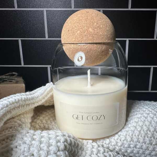 White candle in a glass jar with a cork lid and knitted wrap