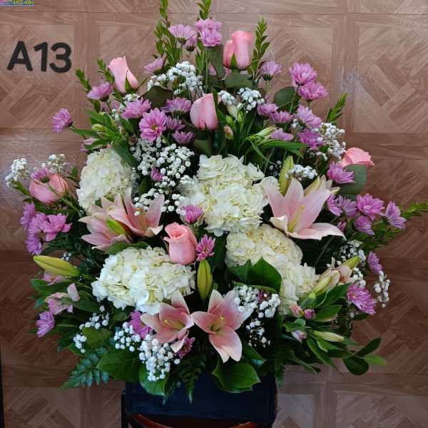 Large pink and white floral arrangement with lilies, roses, hydrangeas, and purple daisies