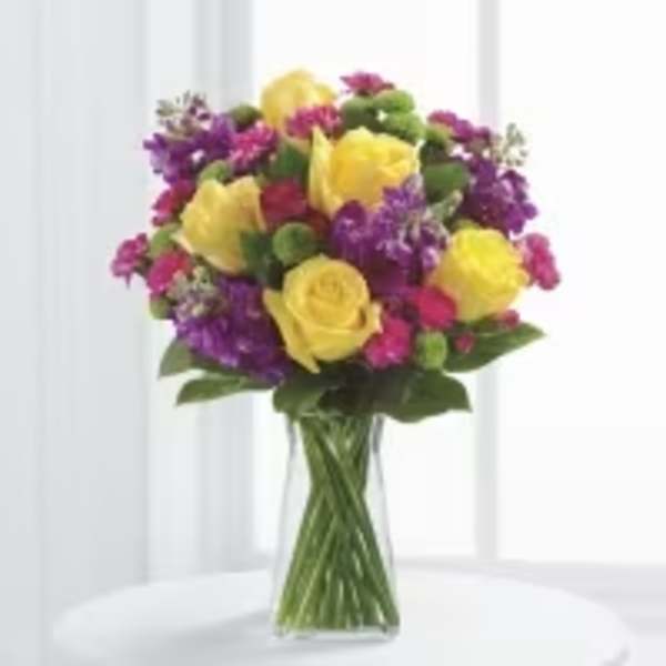 Bouquet of yellow roses and purple flowers in a clear glass vase