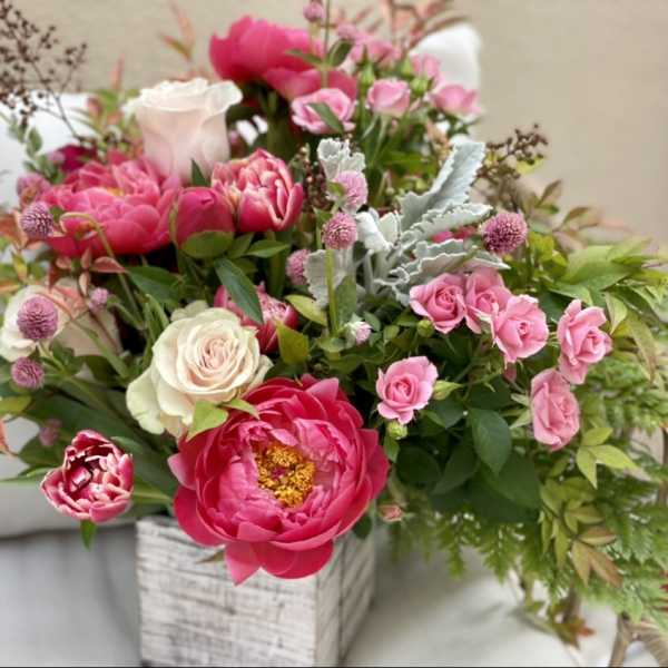 Pink peonies and roses arranged in a whitewashed wooden box