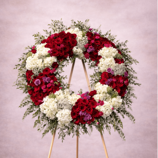 Large standing wreath of red and white flowers with greenery on a wooden easel.
