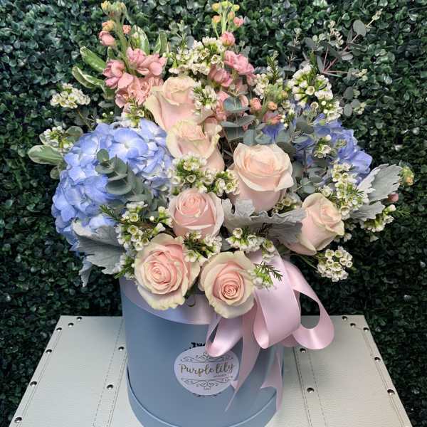 Pastel bouquet of roses, hydrangeas, and small white blooms in a blue hat box
