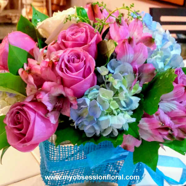 Pink roses and blue hydrangeas in a blue basket with ribbon