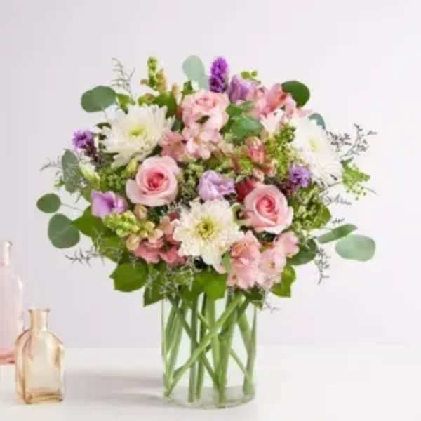 Rounded bouquet of pink roses, white mums, and pastel blooms in a clear glass vase