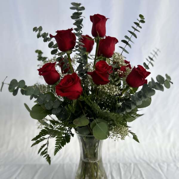 Tall arrangement of red roses with eucalyptus and white filler flowers in a clear glass vase