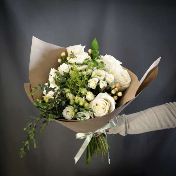 Bouquet of white roses and small white blooms wrapped in brown paper