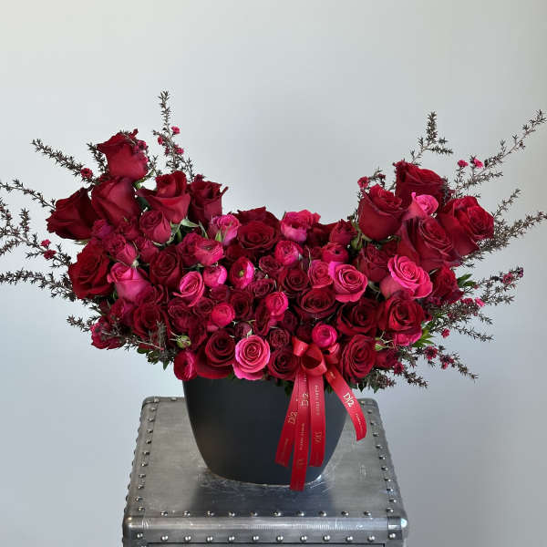 Red and pink rose arrangement in a black vase with ribbon