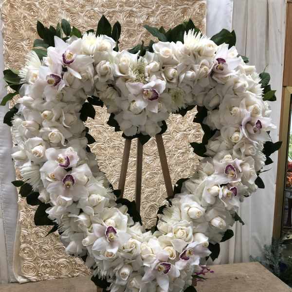 Heart-shaped white floral wreath on an easel with orchids and roses